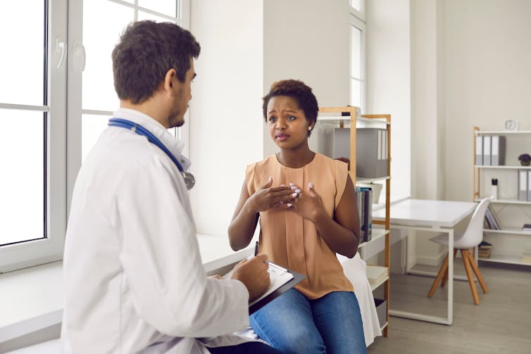 A young black woman speaks with a male doctor about her concerns.