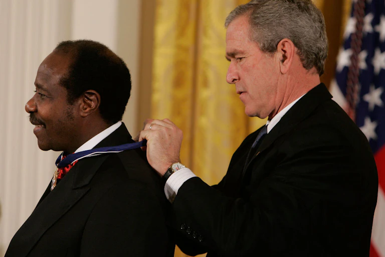 A man tying a ribbon around another man's neck, with the American flag behind them