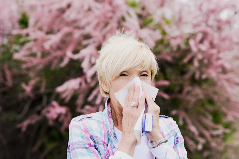 A woman blows her nose in front of a pink tree.