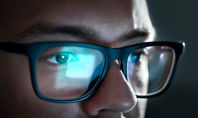 Close up of a young man's eyes, with a computer screen reflected in his glasses