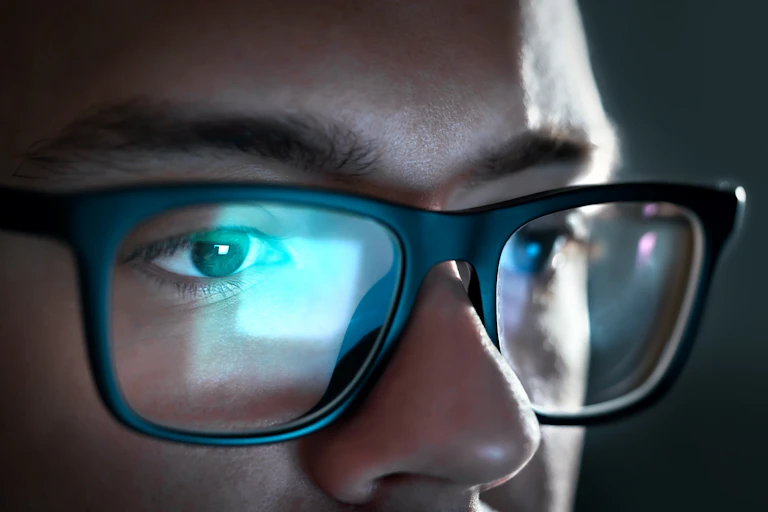 Close up of a young man's eyes, with a computer screen reflected in his glasses