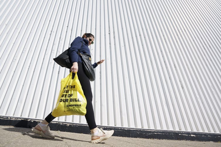 A woman walks with a plastic bag of groceries.