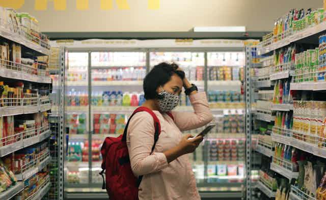A woman has her hand on her head looking at items in a grocery store.