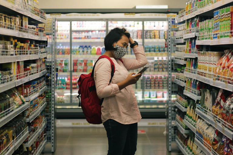 A woman has her hand on her head looking at items in a grocery store.