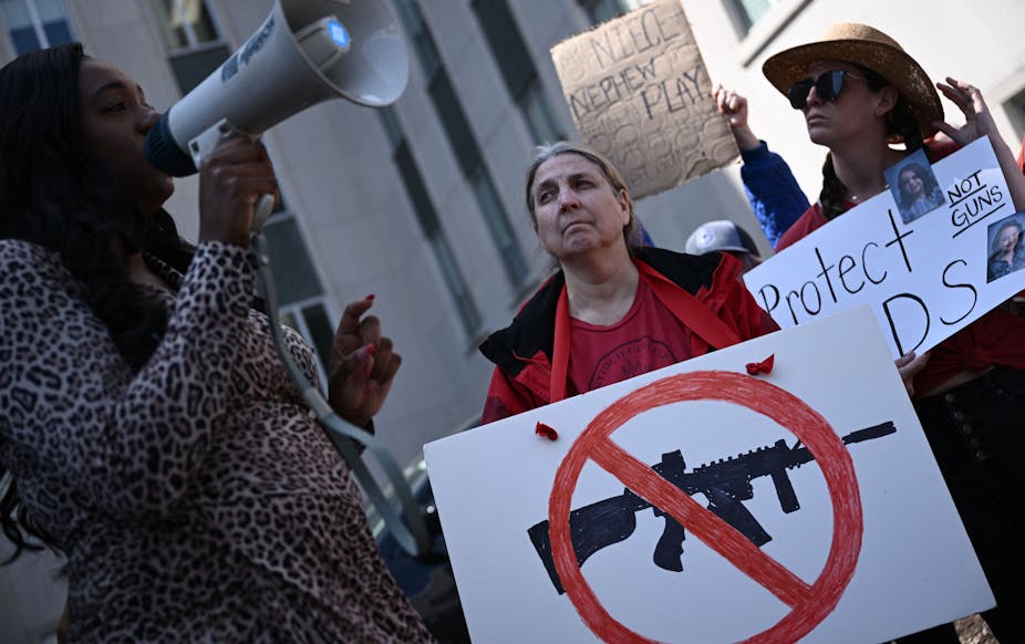 A woman holds a placard with a drawing of an assault rifle and a red diagonal line through it.