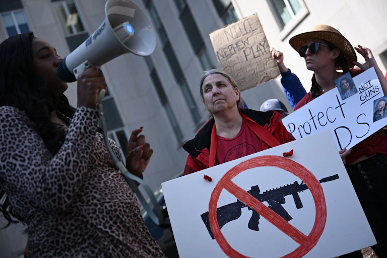 A woman holds a placard with a drawing of an assault rifle and a red diagonal line through it.
