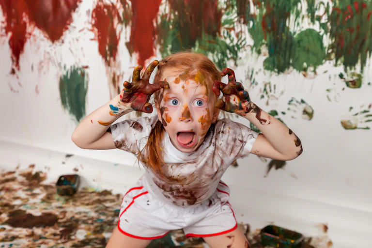 A kid painted herself and with the background wall also painted in different colors.
