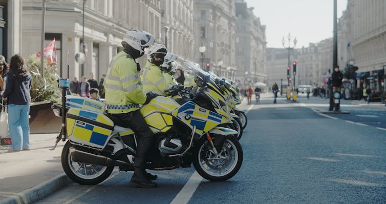 Several police officers in uniform on police motorbikes by a street curb.