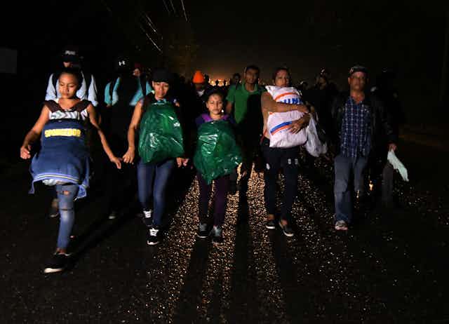 Men, women and children, some with their bagged possessions strapped to their bodies, walk at night from Honduras on their way to the United States.