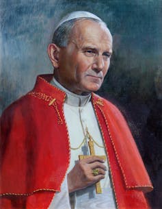 Portrait of John Paul II wearing a red cape and holding a wooden crucifix.