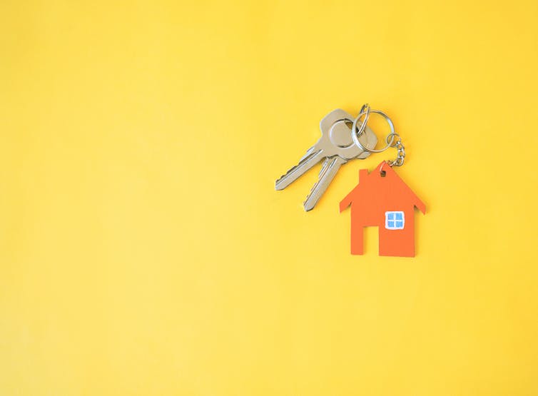 Two silver keys on an orange house keyring, on a yellow background.