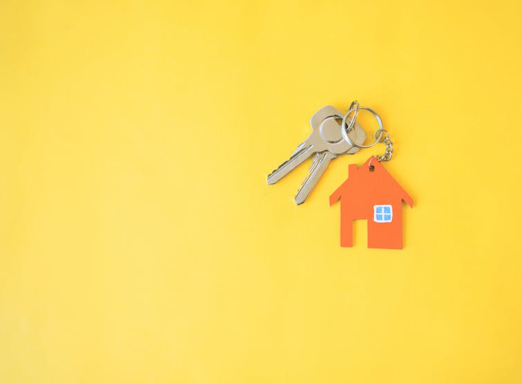 Two silver keys on an orange house keyring, on a yellow background.