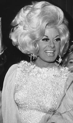 Danny La Rue dressed as a woman in a fabulous blonde wig and spangly dress.