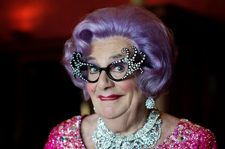 Dame Edna Everage in full regalia of purple wig, pussy cat specs and lots of jewellery and sequins.