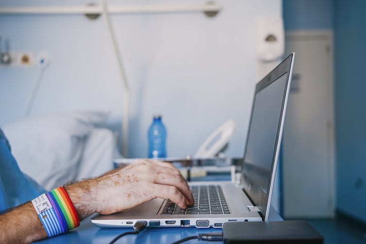 Close-up of hands of patient using laptop, wearing rainbow band.