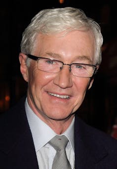 The TV presenter Paul O'Grady dressed in a black suit, white shirt and grey tie.