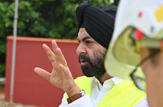 A man wearing a traditional  Sikh turban gestures while speaking to workers outside a power plant.