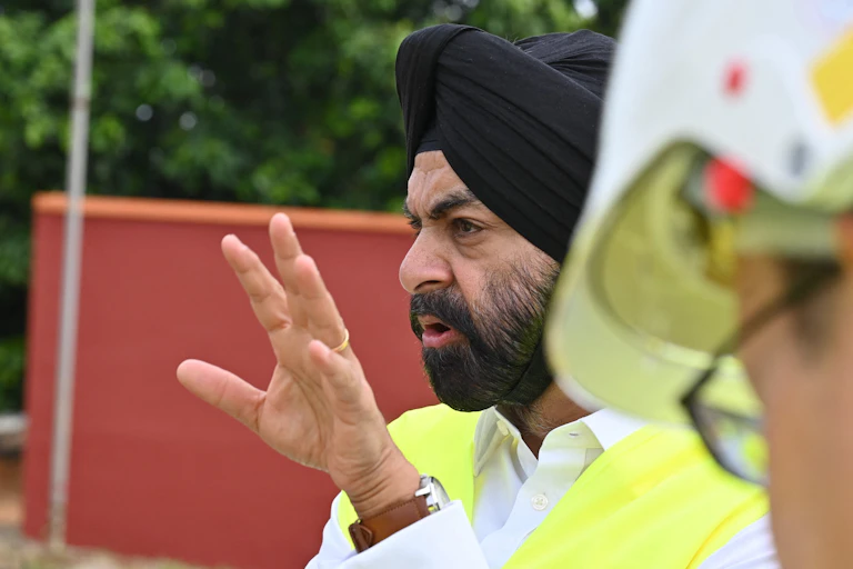 A man wearing a traditional Sikh turban gestures while speaking to workers outside a power plant.