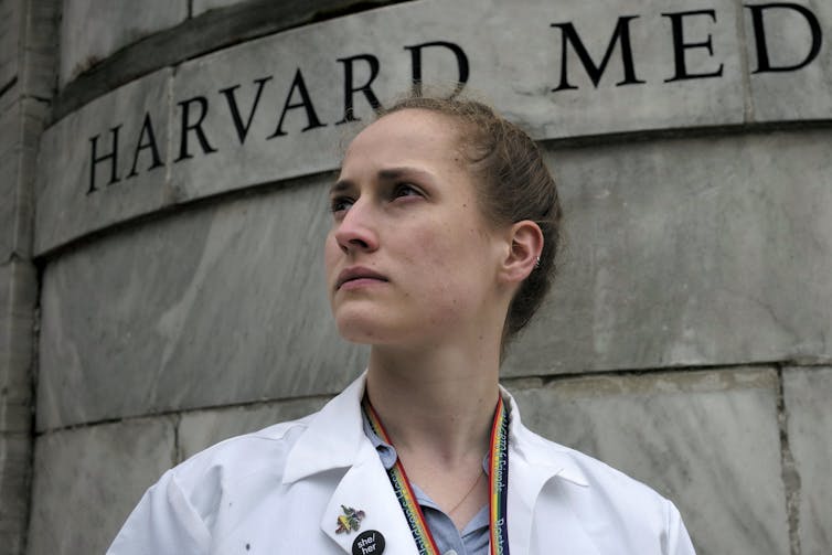 Medical student wearing rainbow lanyard in front of Harvard Medical School building
