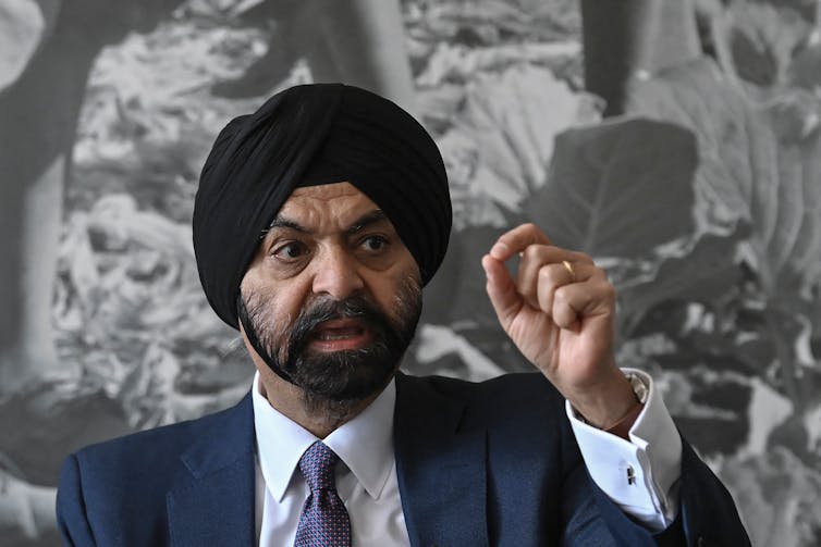 Ajay Banga, wearing a traditional Sikh turban and business suit, gestures as he speaks in front of a photo of workers picking vegetables.