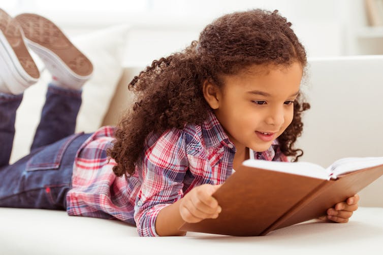 a child lying on the floor reads from a book