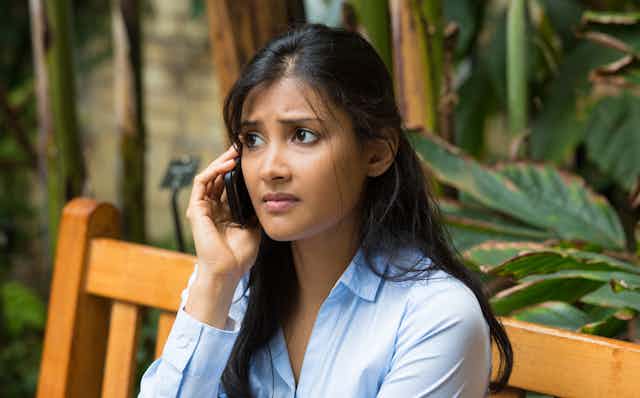 Worried woman sitting on outside bench with mobile phone to ear