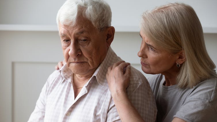 Older woman comforting older man, hands on his shoulders
