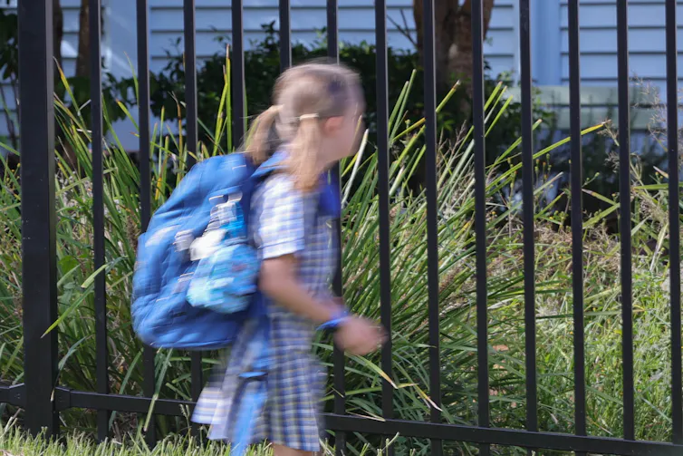A school student walking outside the school fence.