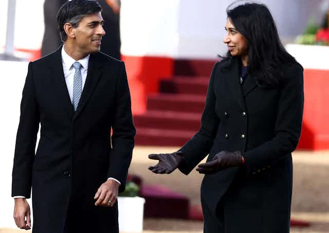 Rishi Sunak and Suella Braverman standing and chatting to each other at an outdoor event, both wearing formal clothing and black, wool coats
