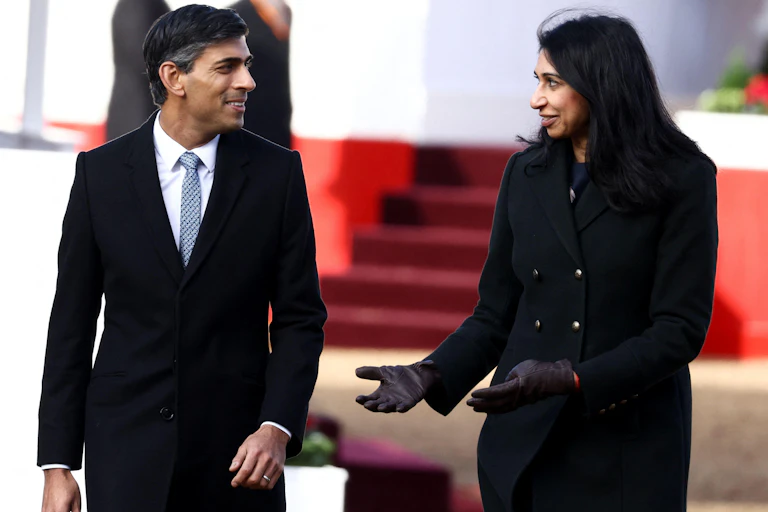 Rishi Sunak and Suella Braverman standing and chatting to each other at an outdoor event, both wearing formal clothing and black, wool coats