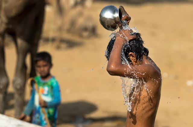 Niño se vierte agua encima desde un recipiente de metal.