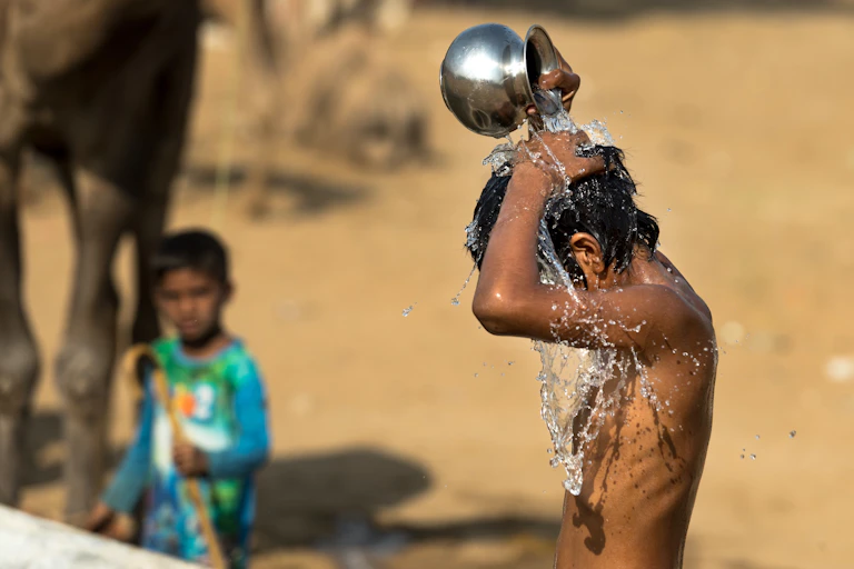 Niño se vierte agua encima desde un recipiente de metal.