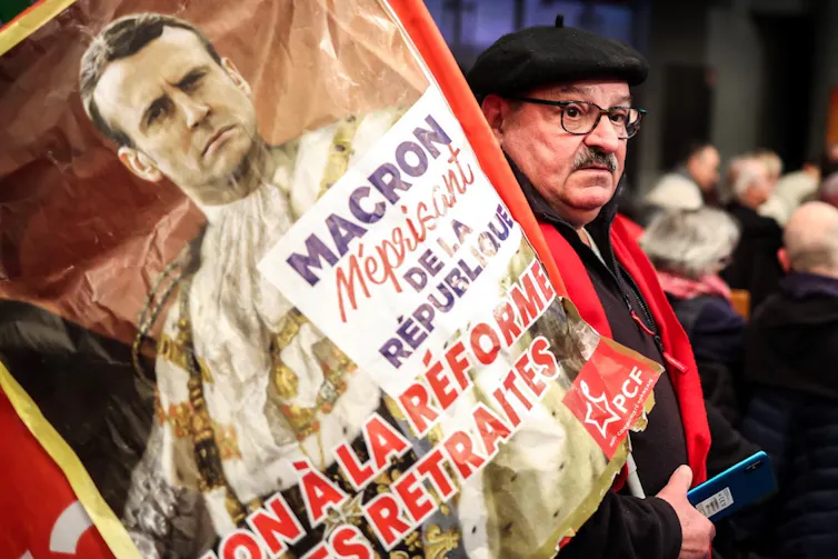 A beret-clad older worker holds a sign