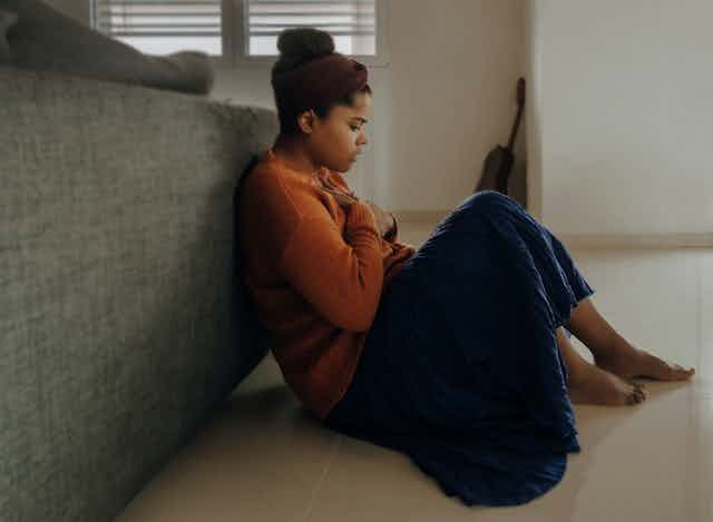 African-Australian woman sits on the floor, feeling anxious