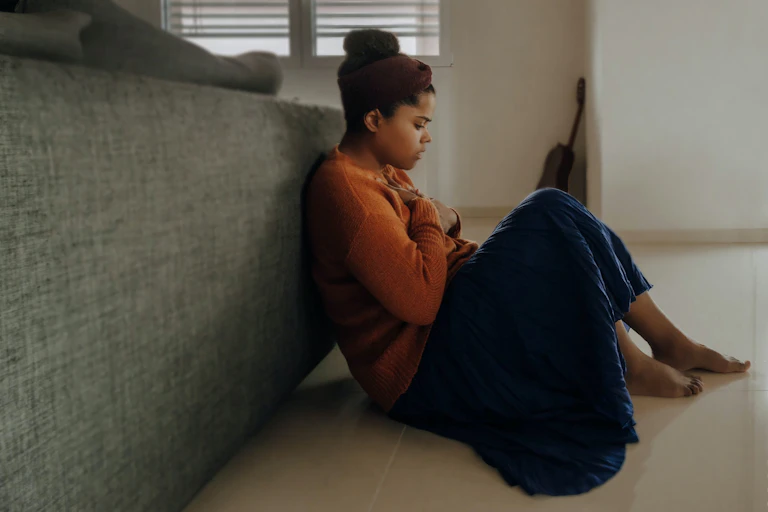 African-Australian woman sits on the floor, feeling anxious