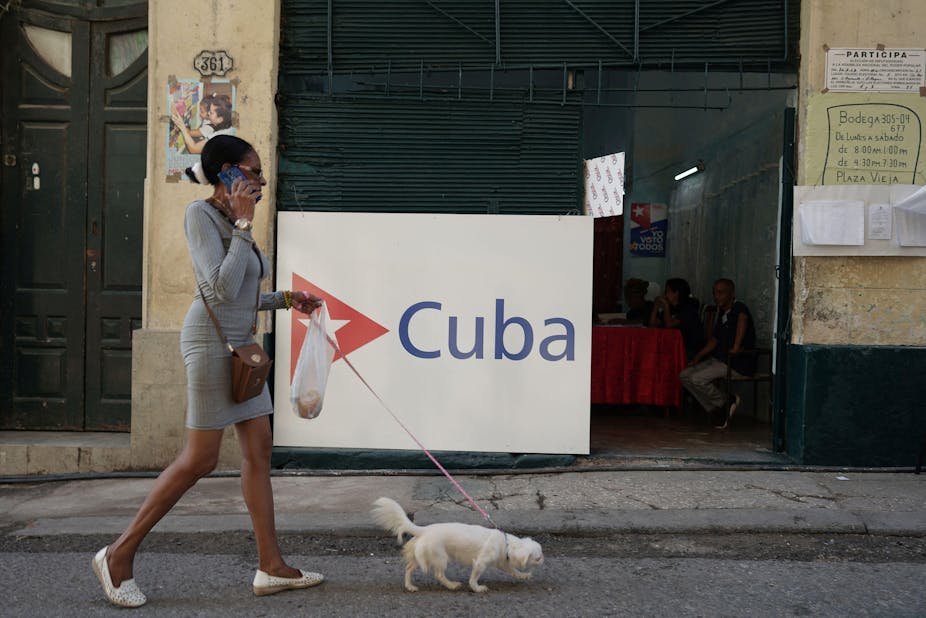 A woman talks on the phone and has a dog on a lead as she walks along a Havana street.