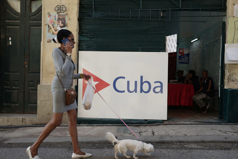 A woman talks on the phone and has a dog on a lead as she walks along a Havana street.