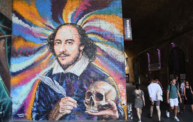 A mural of Shakespeare painted over a whirlwind of colours. He holds a feather quill and a skull. 
