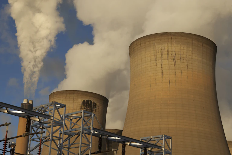 Smoke and steam spewing from a narrow chimney and two cooling towers.