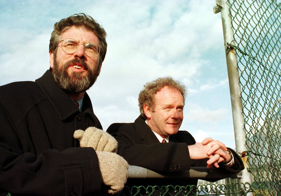 Gerry Adams and Martin McGuinness leaning on a fence looking relaxed. 