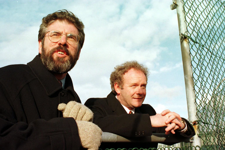 Gerry Adams and Martin McGuinness leaning on a fence looking relaxed.