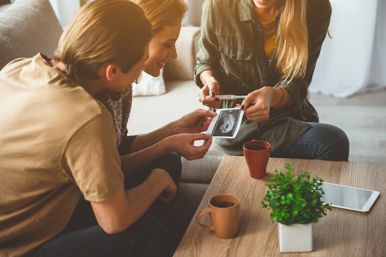 Couple receiving ultrasound picture from surrogate expectant mother.