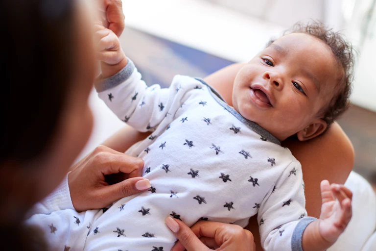 A baby seen looking up into the face of a parent and smiling.