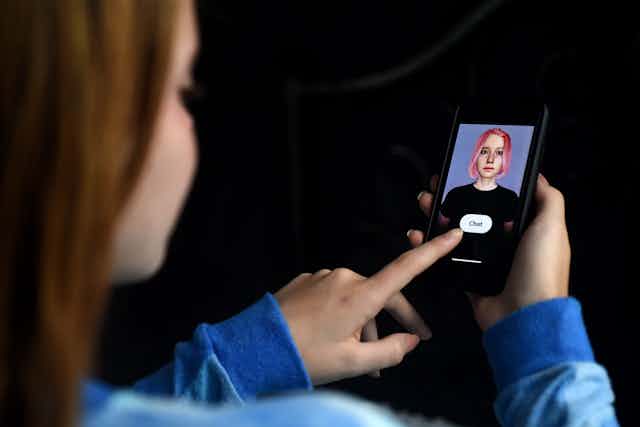 Girl about to press a 'chat' button on her smartphone, which has a pink-haired avatar displayed on the screen.