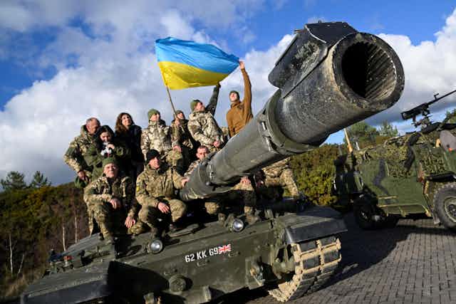 Ukrainian and British troops on a Challenger tank with a Ukraine flag.