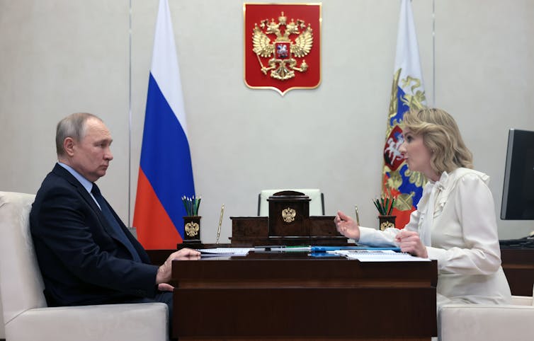 Vladimir Putin sits at his desk in the Kremlin facing Russia's children's rights commissioner, Maria Lvova-Belova.