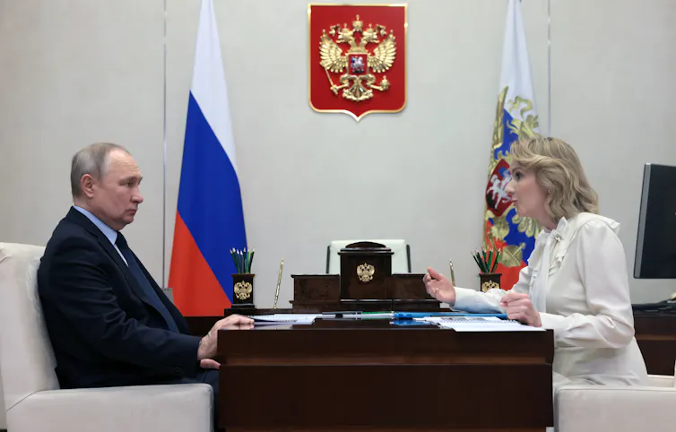 Vladimir Putin sits at his desk in the Kremlin facing Russia's children's rights commissioner, Maria Lvova-Belova.