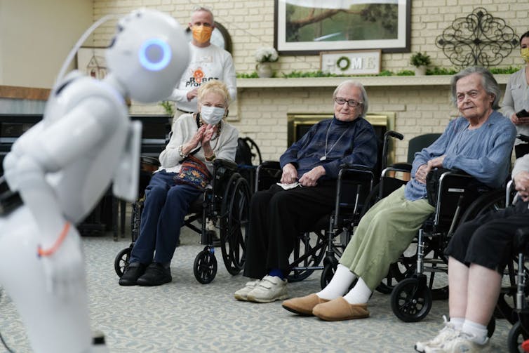 Elderly people in wheelchairs watch a white robot.
