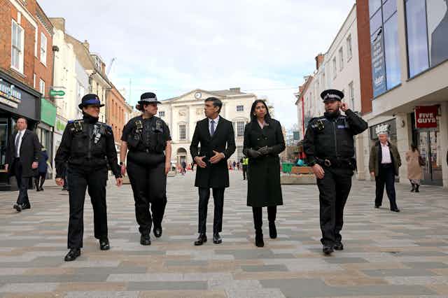 Rishi Sunak and Suella Braverman walking along a high street with three police  officers.