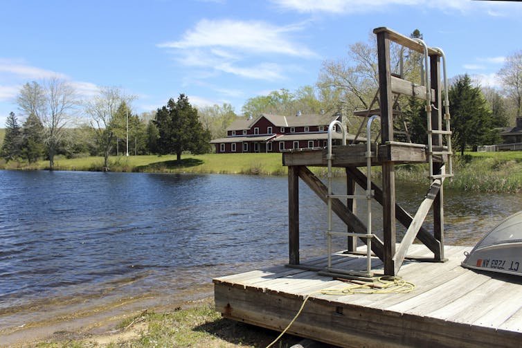 A lakeside structure in the wilderness with a large rustic building in the background.